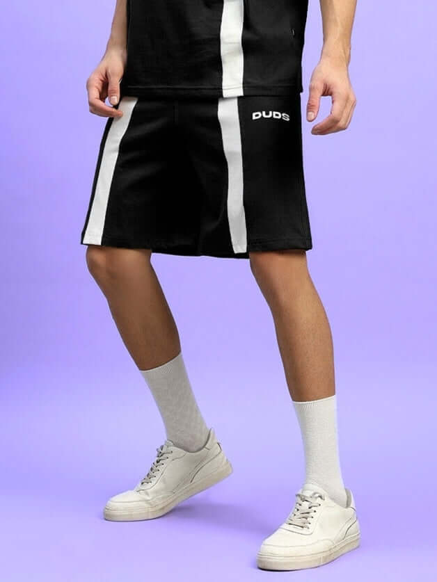 Person wearing WIDELINE regular fit black shorts by DUDS with white side stripes, showcasing casual style against a vibrant backdrop.