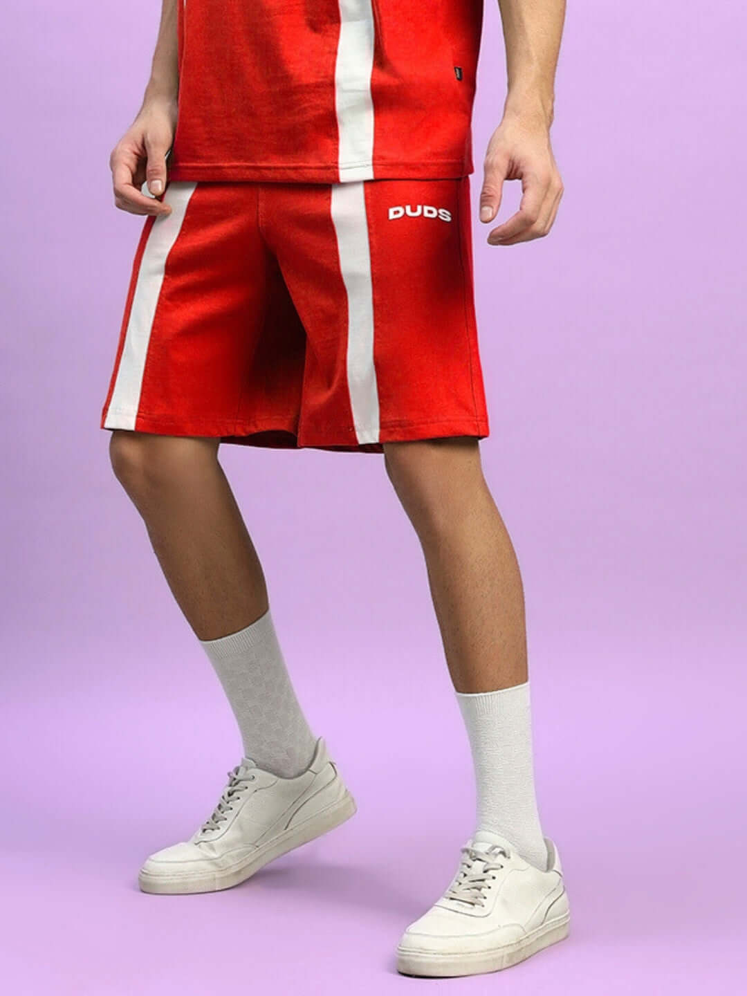 Man wearing red Wideline regular fit shorts with white stripes and white sneakers, by DUDS, on a purple background.