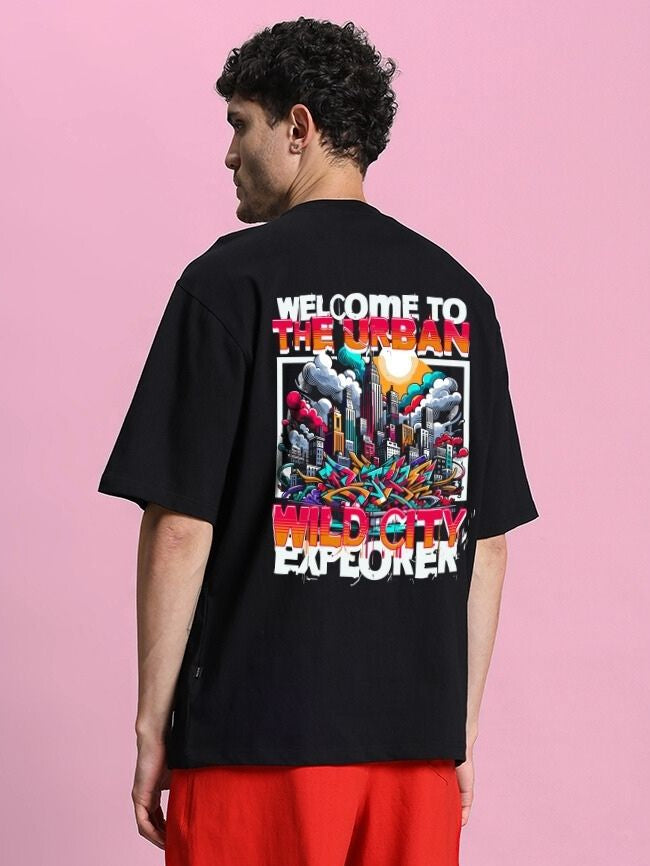 Back view of WILD CITY OVERSIZED T-SHIRT BLACK with urban graphic design against a pink background