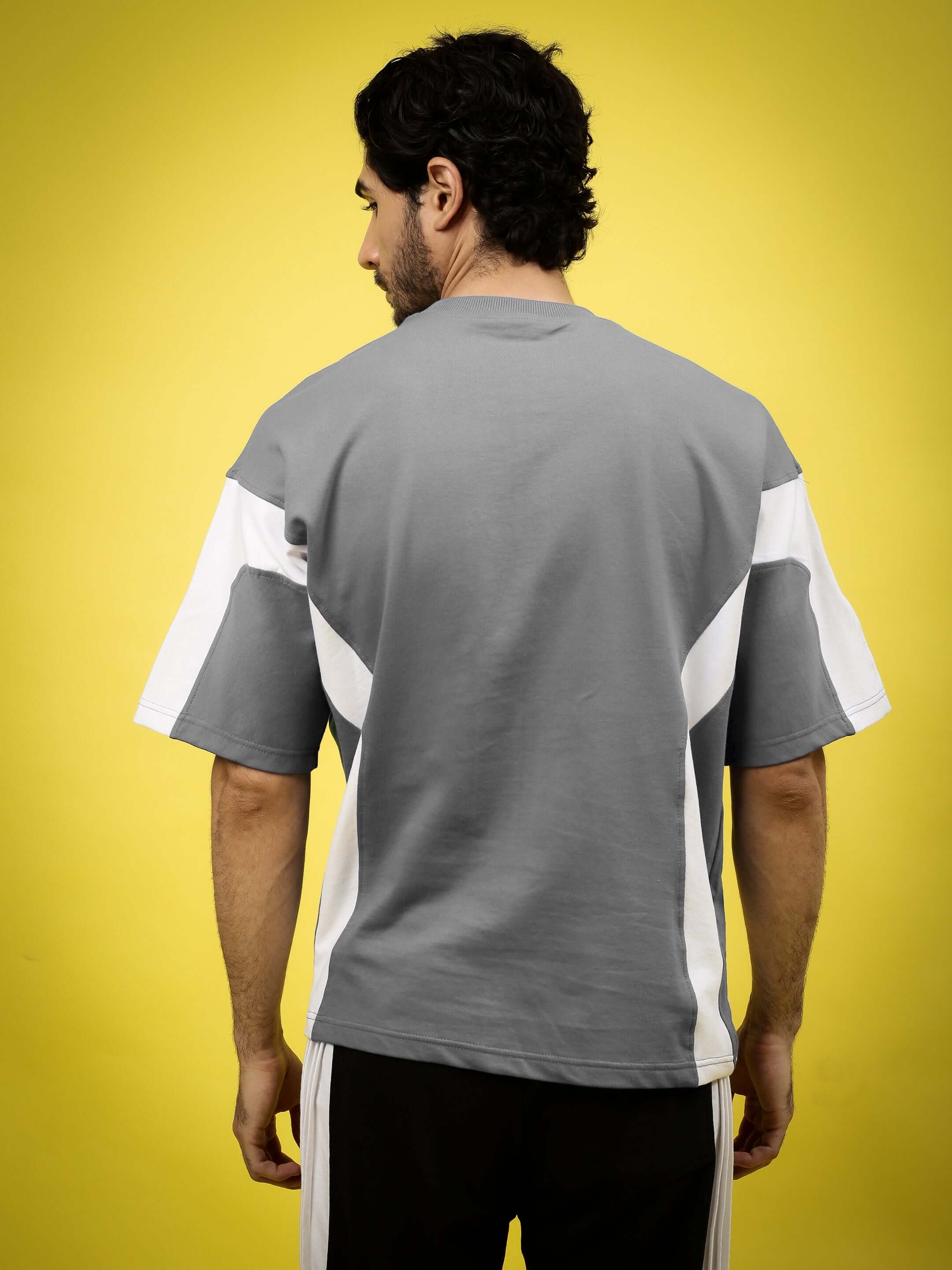 Back view of WILD FORCE oversized grey-white T-shirt made from premium cotton and elastane, modeled by a person against a yellow background.