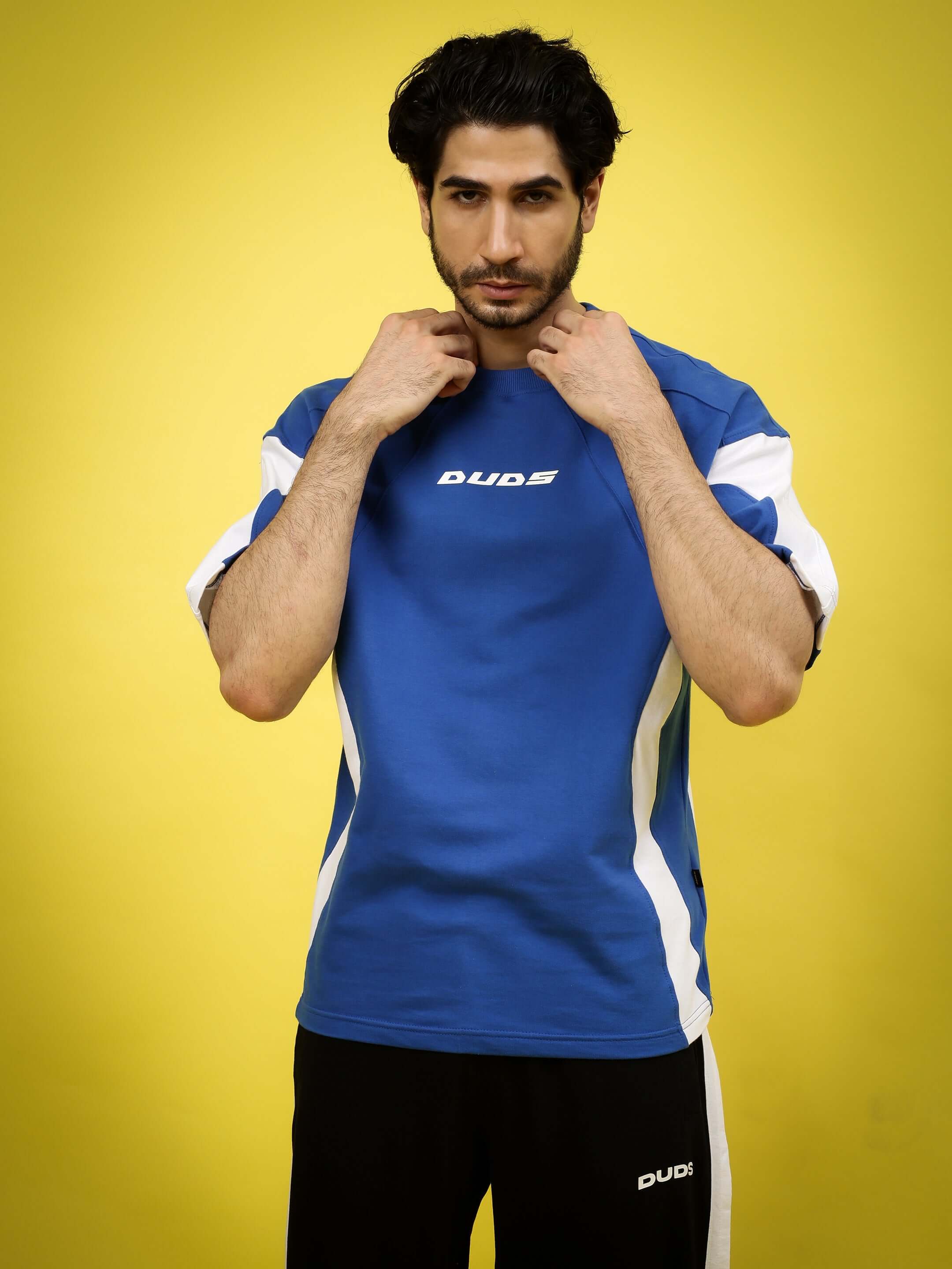 Model wearing premium WILD FORCE over-sized t-shirt in royal blue-white, made of 97% cotton French terry, against yellow background.