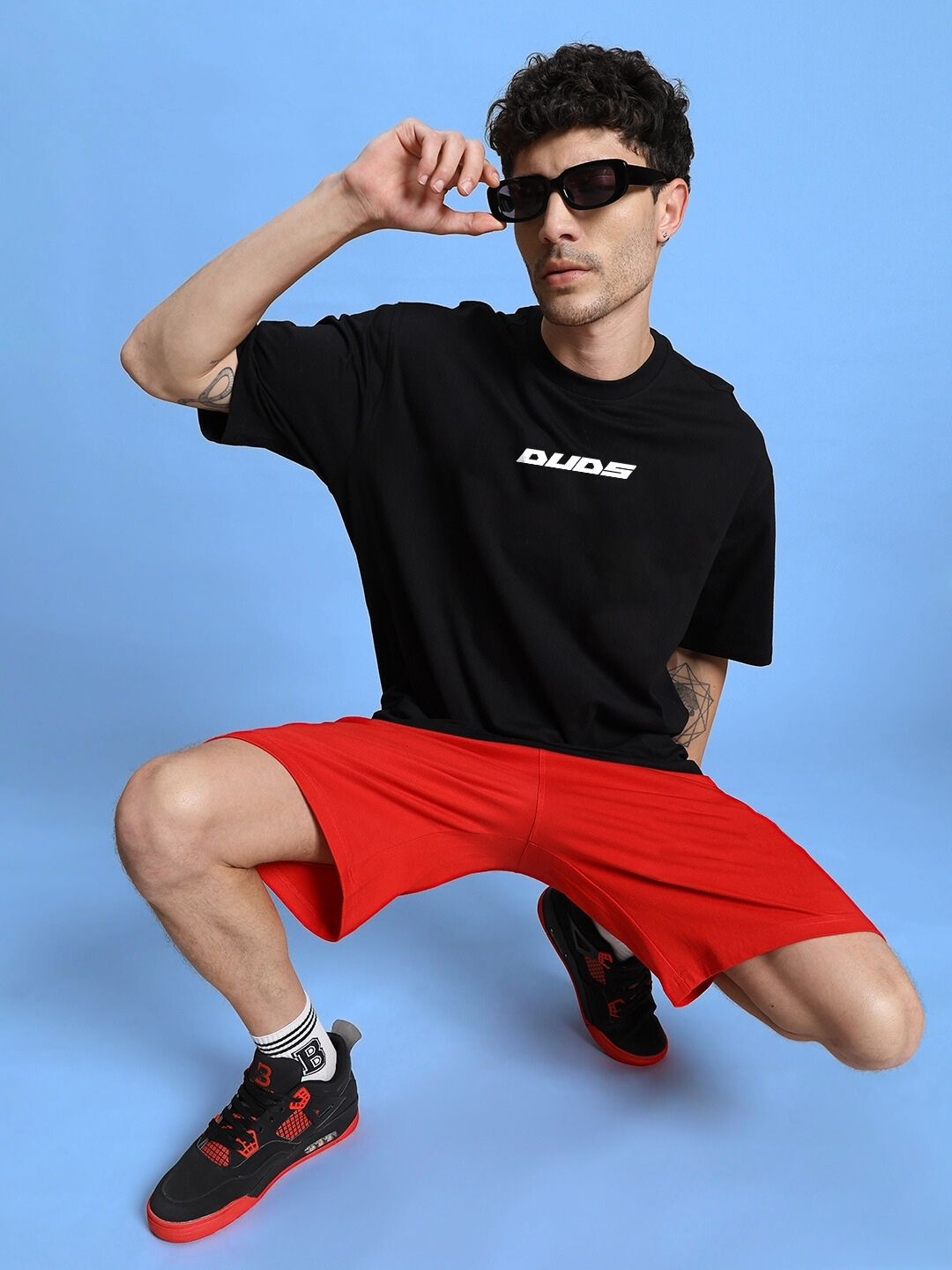 Model wearing WINGED WARRIOR PRINTED OVERSIZED CO-ORD SET BLACK RED, in a bold street-style pose against a blue background.