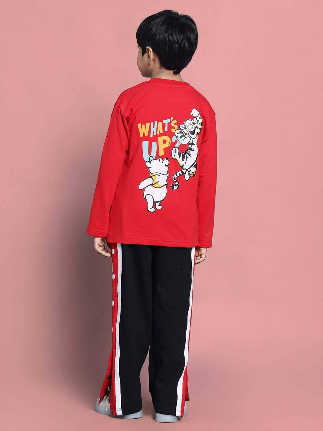 Child wearing red and black WINNIE CO-ORD set with cartoon design on back, standing against a pink background.