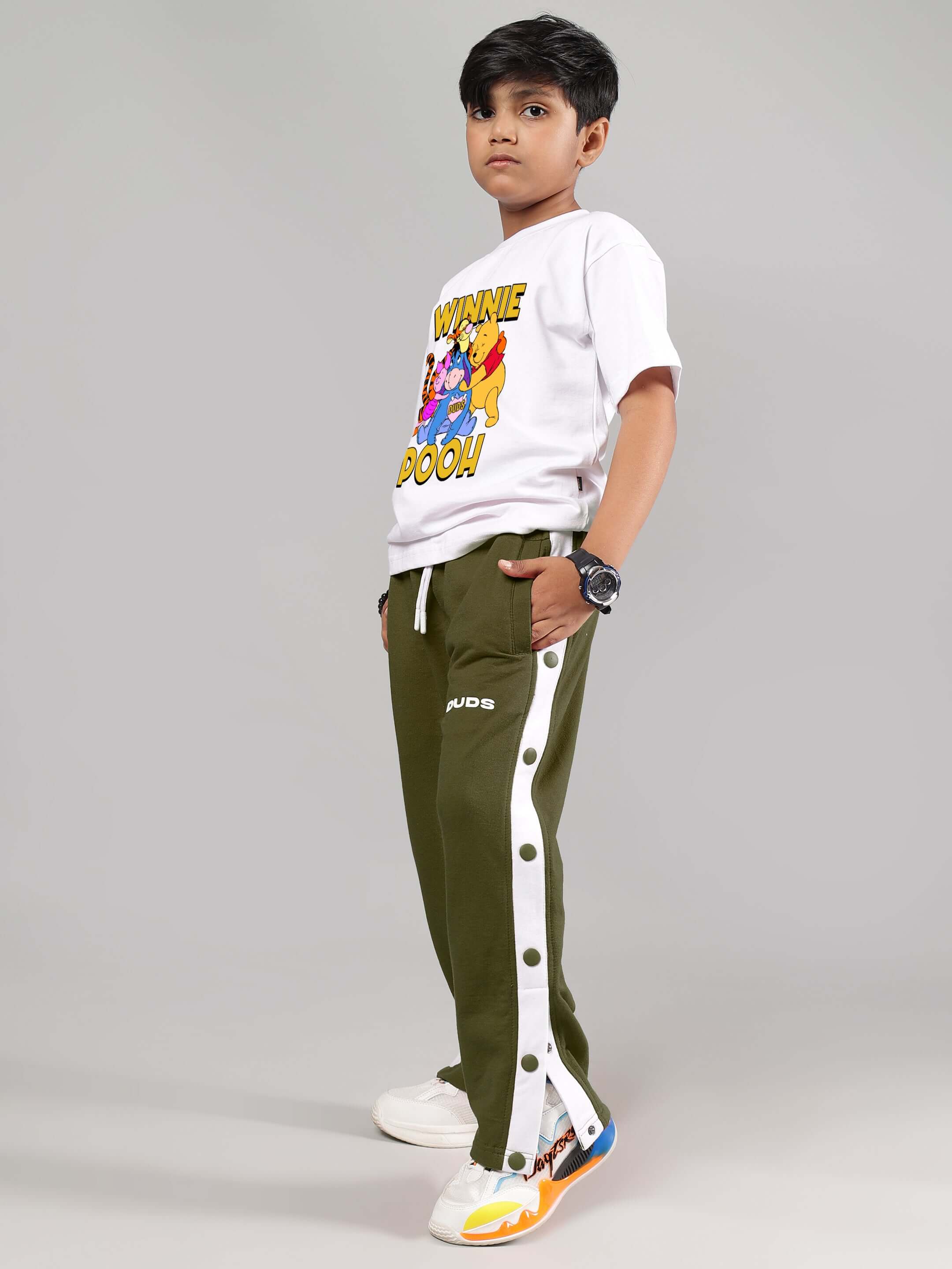 Child wearing Winnie the Pooh co-ord set in white and olive-green with printed top and buttoned pants, ideal for boys and girls.