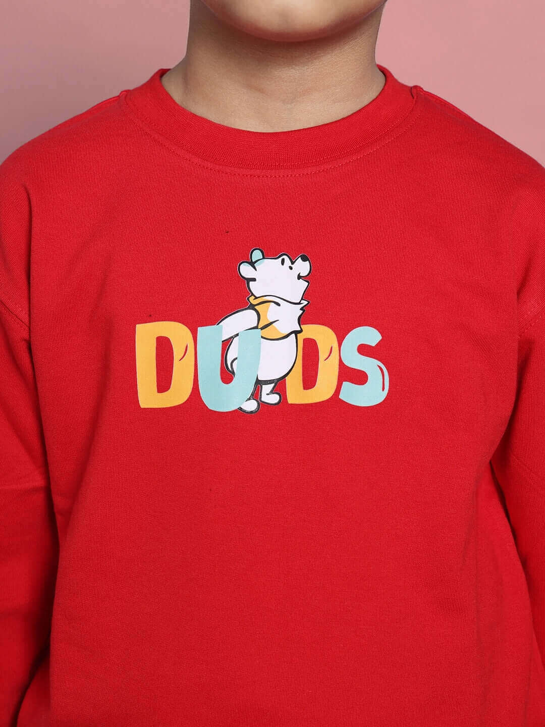 Child wearing a red sweatshirt with cartoon bear and colorful 'DUDS' print, showcasing children's fashion co-ord by DUDS.