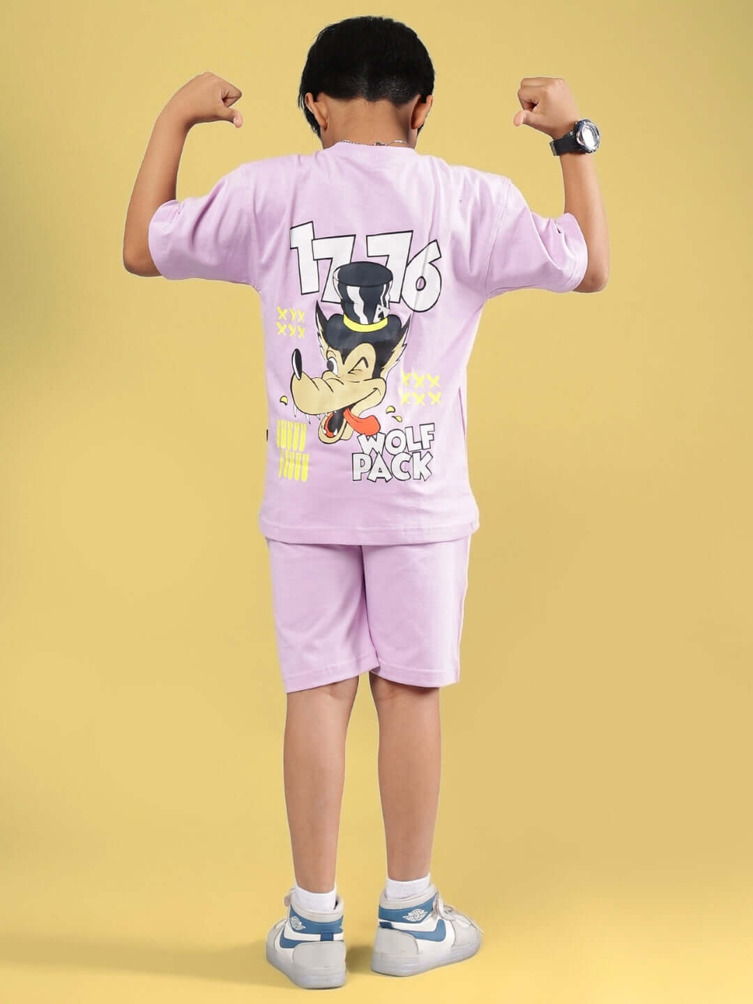 Child wearing WOLF PACK CO-ORD FOR BOYS & GIRLS LILAC, lilac outfit showing a cartoon graphic on the back, yellow background.