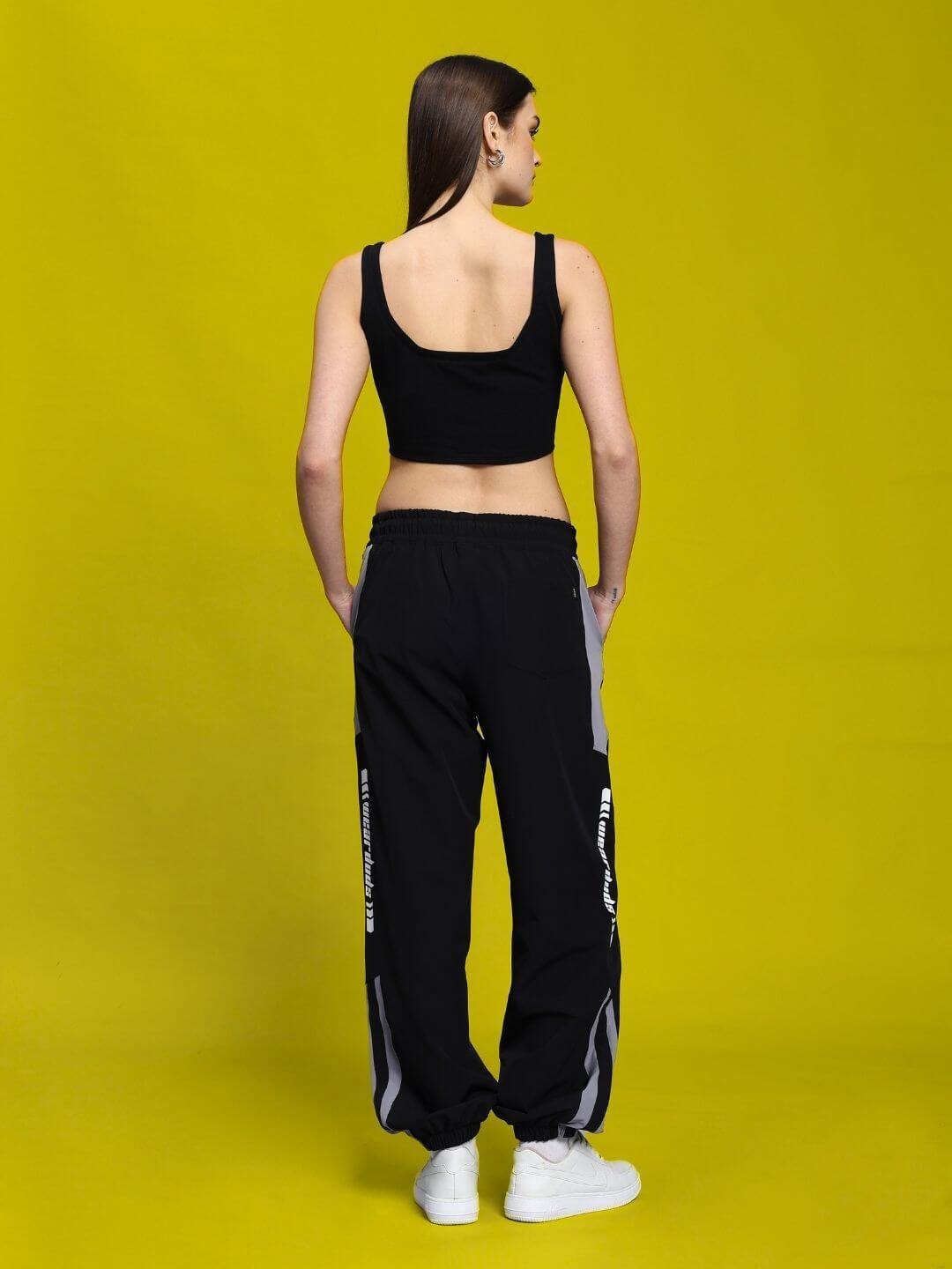 Back view of model wearing WOMEN'S DANNY RELAXED FIT CARGO PANTS BLACK against yellow background.