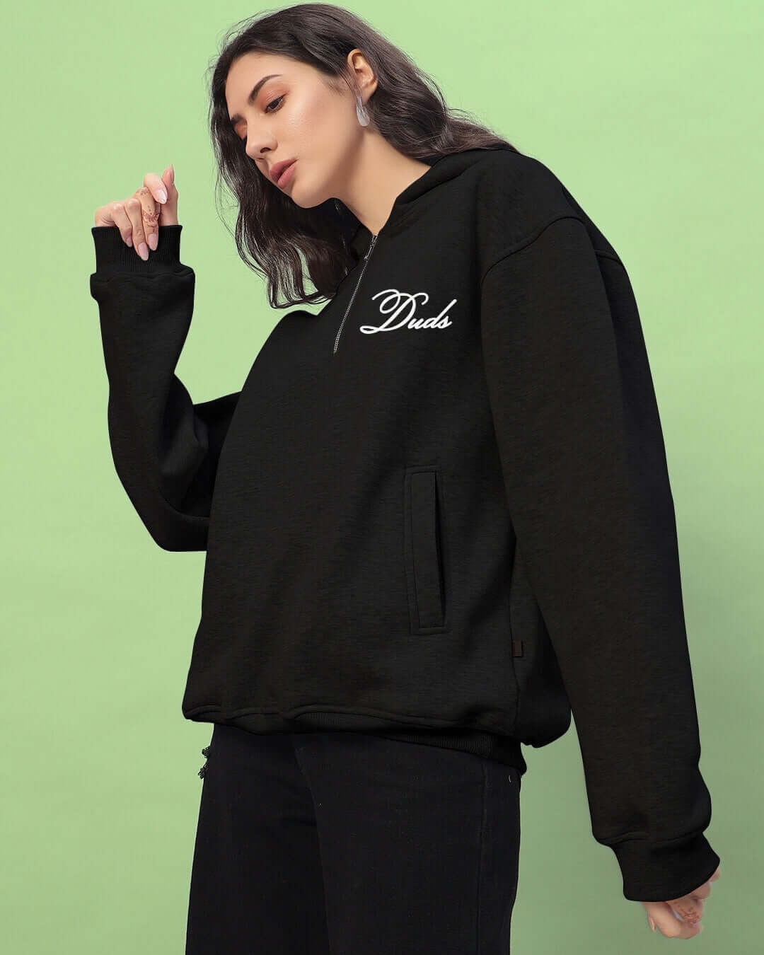 Woman wearing black Amarillo fleece hoodie by DUDS with a green background.