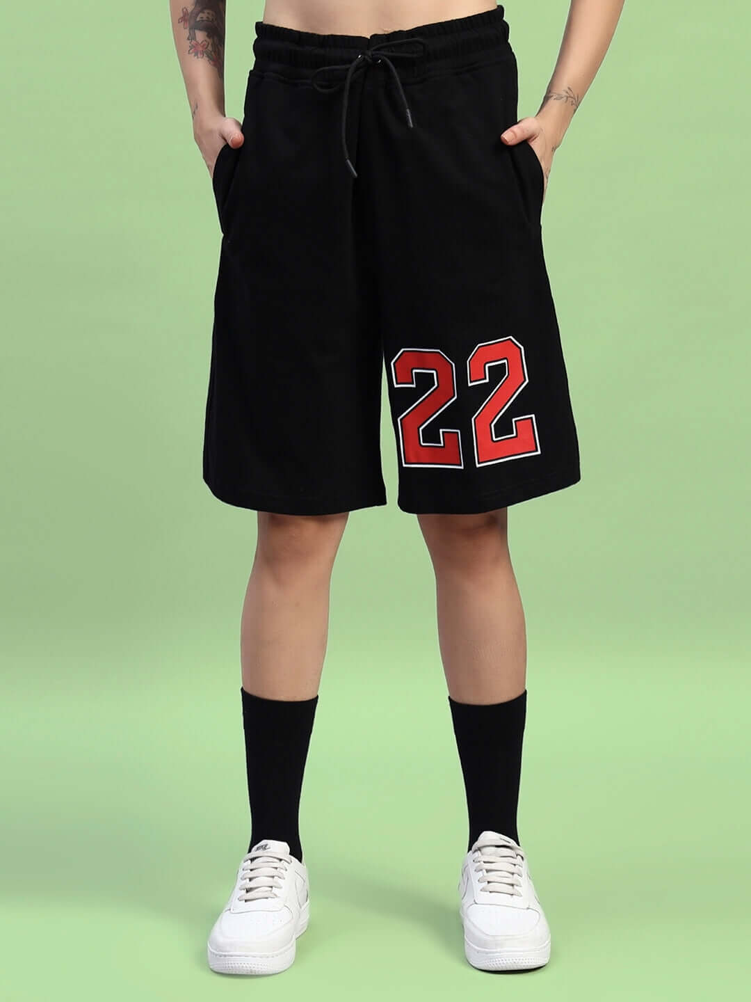 Model wearing women's black regular fit shorts with red '22' print, showcasing a casual look with white sneakers and black socks.