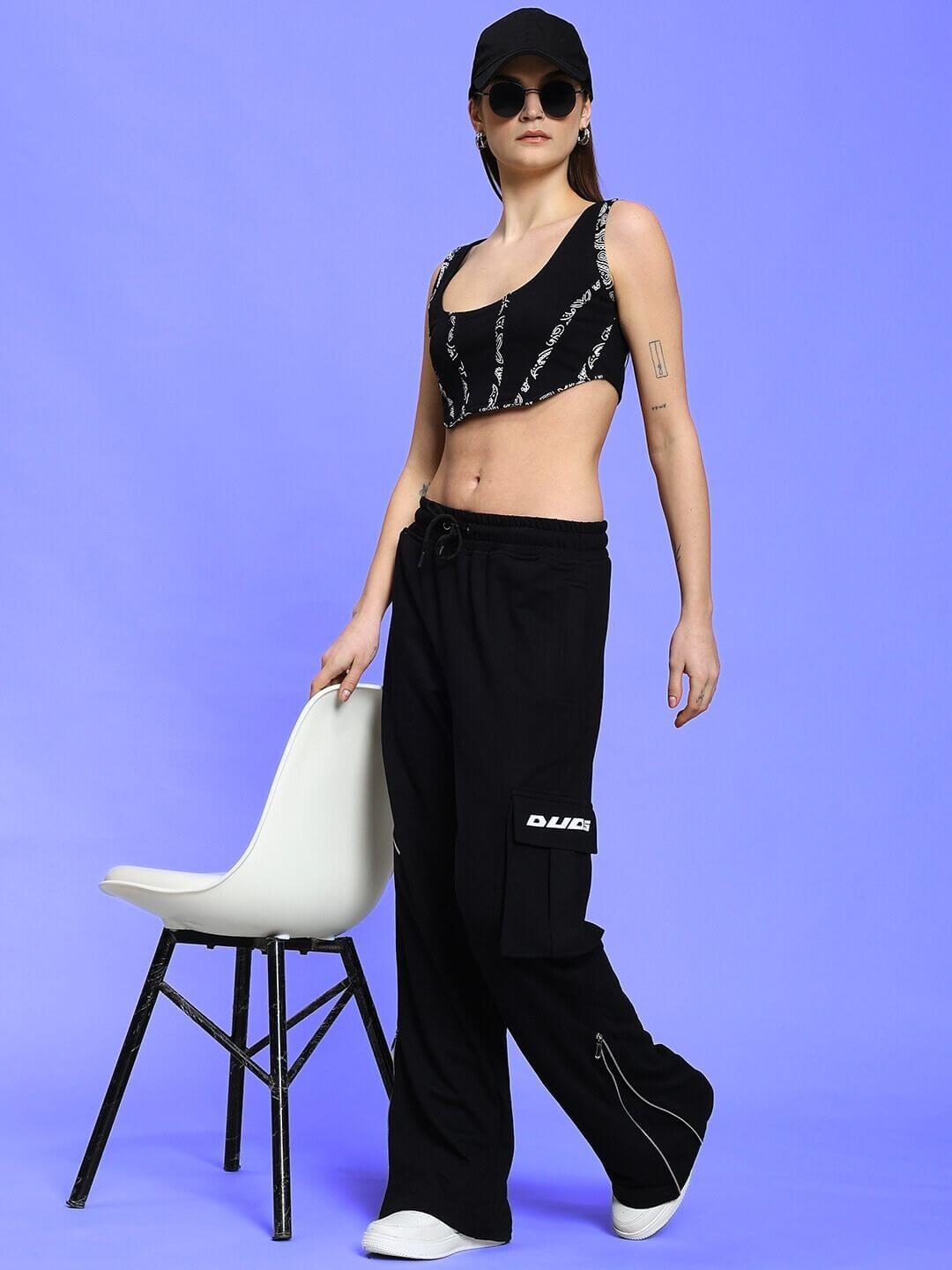 Woman in black Amisha co-ord set with relaxed fit joggers, showcasing fashion style against a purple background, next to a white chair.