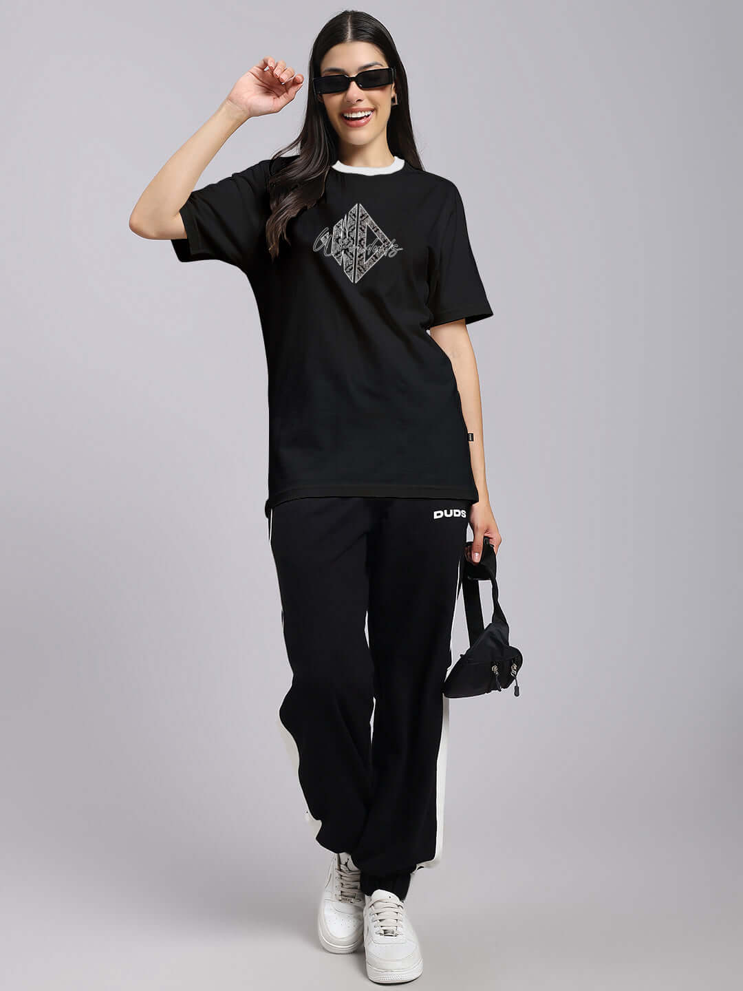 Woman wearing black regular fit angular T-shirt, styled with sunglasses and matching pants, emphasizing casual elegance and comfort.