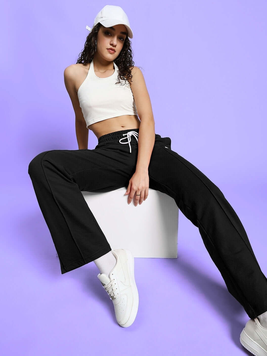 Woman in black-off white Anissa Co-ord Set, relaxed fit joggers with elastic waistband, styled with white sneakers on a purple backdrop.