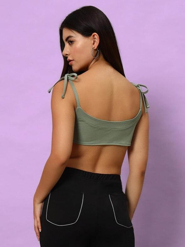 Model wearing laurel green Ashley crop-top made from polyester and spandex, showcasing back tie straps against a lilac backdrop.