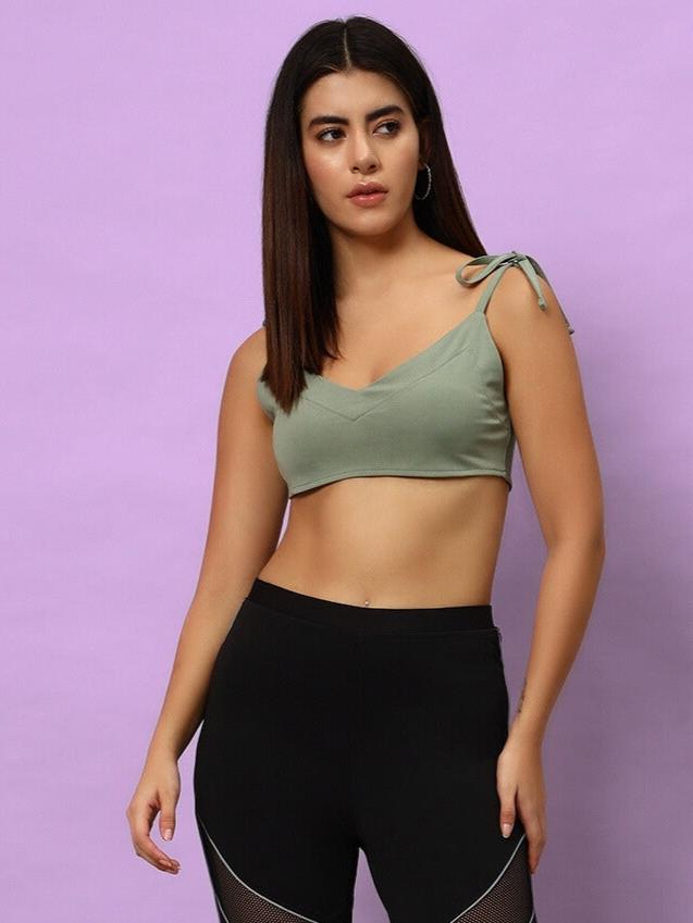 Model wearing women's Ashley crop-top in laurel green, made of polyester and spandex, styled with black leggings against a purple background.