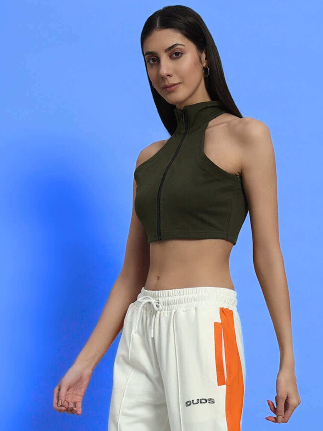 Woman wearing WOMEN'S AURA CROP-TOP - OLIVE GREEN standing against a blue background, showcasing casual and stylish design.