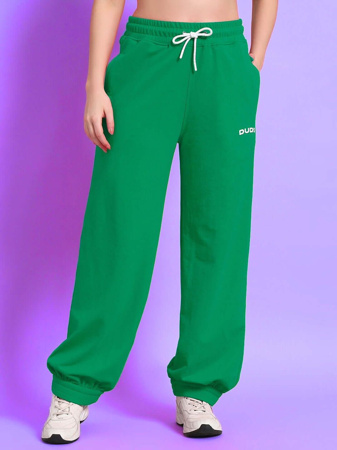 Women's green Austrian relaxed-fit joggers by DUDS, featuring a drawstring waist and custom fit option, showcased on a light purple background.