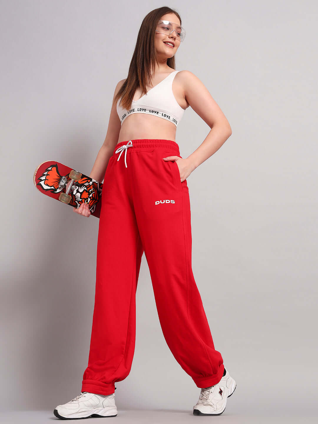 Woman wearing WOMENS AUSTRIAN RELAXED-FIT JOGGERS RED, holding a skateboard, showcasing sporty and bold fashion.
