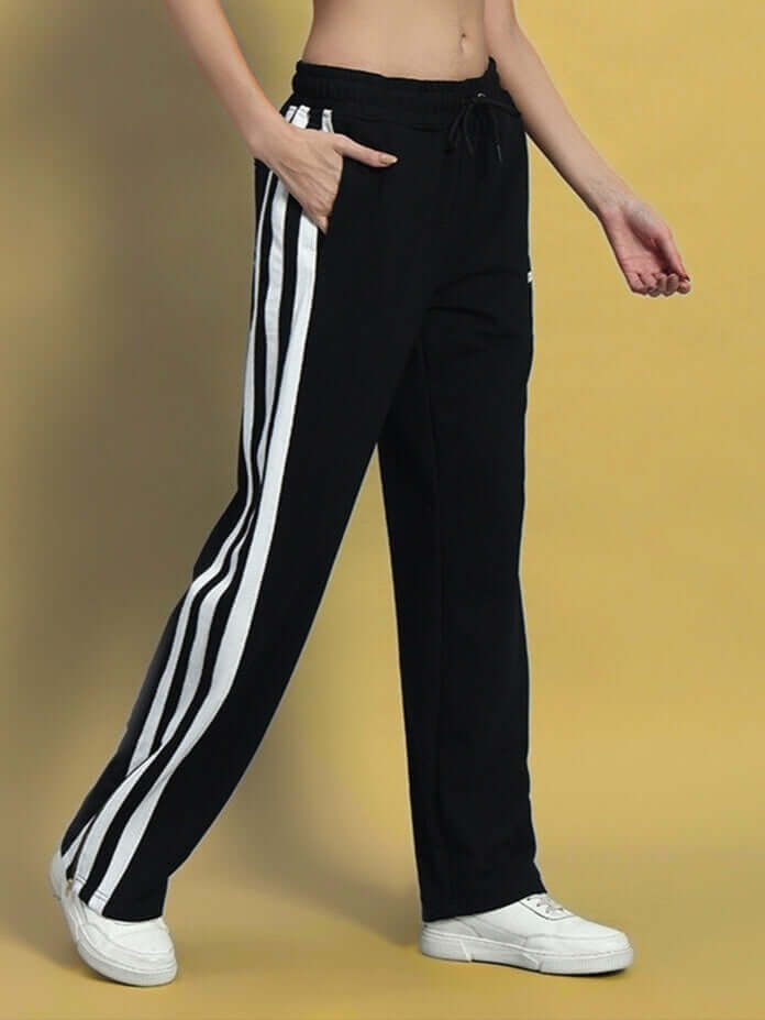 Woman wearing black-white Avalon Slit Zipper Joggers by DUDS, standing against a yellow background showcasing stylish athletic design.