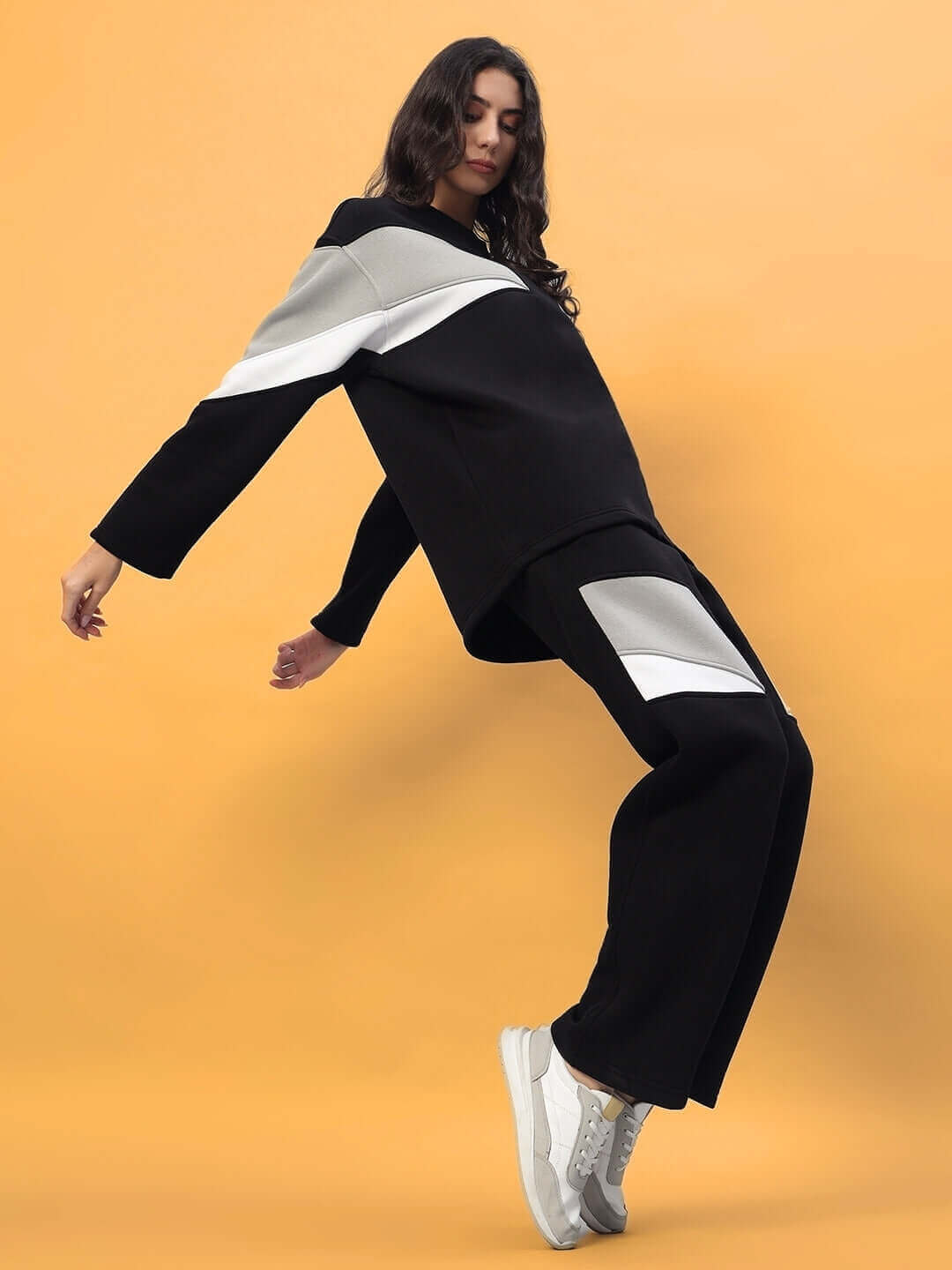 Woman wearing black women's aviator fleece colorblock co-ord, featuring a stylish design with white sneakers, against a warm backdrop.