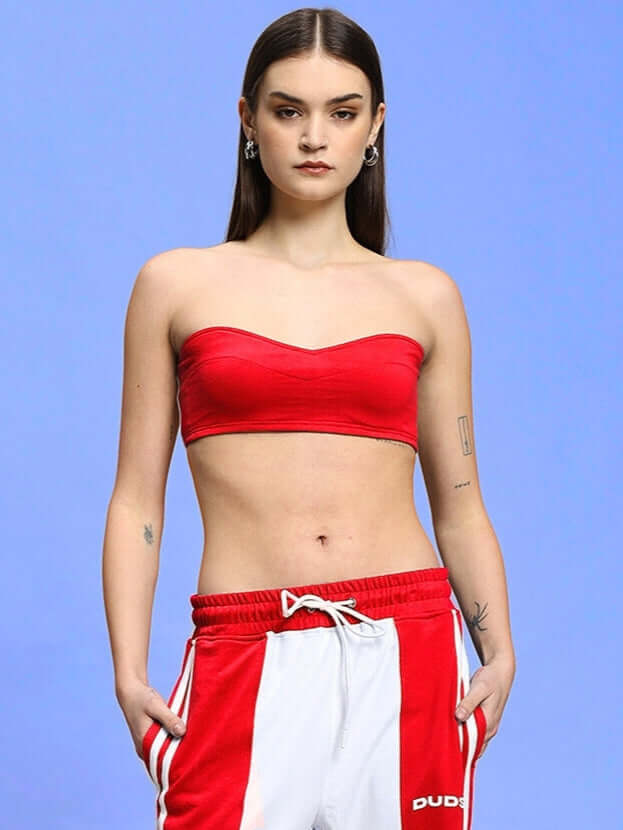 Model wearing red Women's Azora Bandeau Top, 100% cotton, paired with athletic pants, against a blue background.