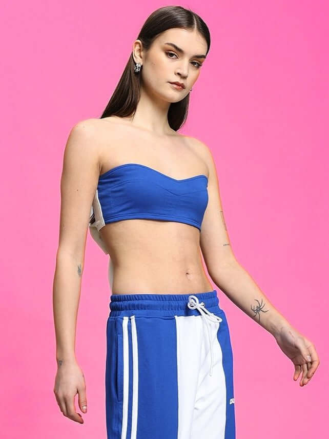 Model wearing Women's Azora Bandeau Top in royal blue, styled with casual blue and white drawstring pants against a pink background.