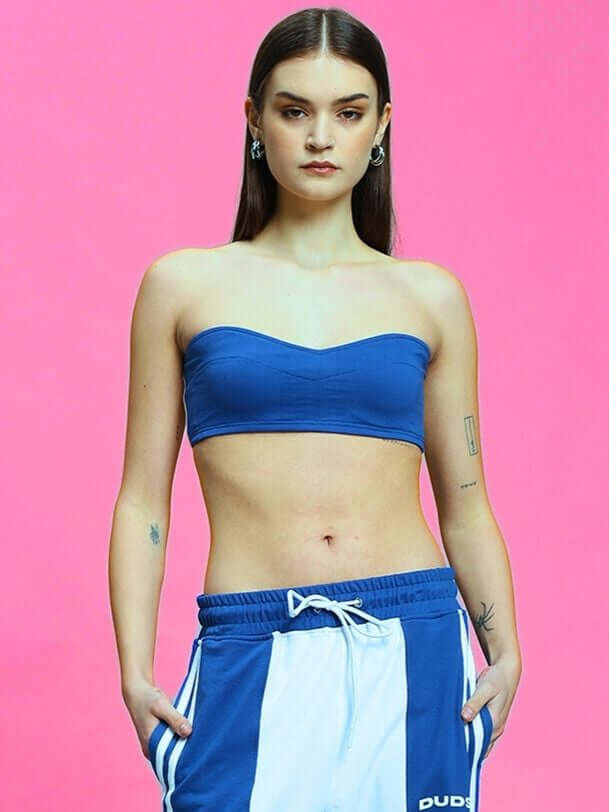 Woman wearing a royal blue bandeau top and blue-striped pants on a pink background.