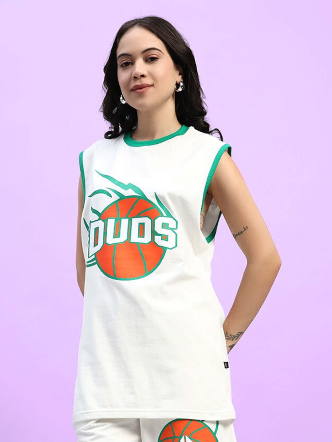 Woman wearing an oversized white t-shirt with green trim and basketball graphic, standing against a pastel purple background.
