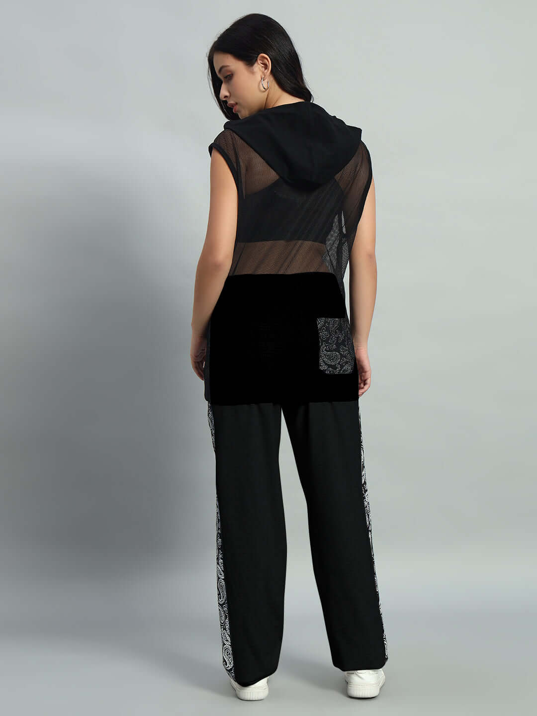 Woman wearing black relaxed fit joggers and sheer sleeveless top, standing with back view.