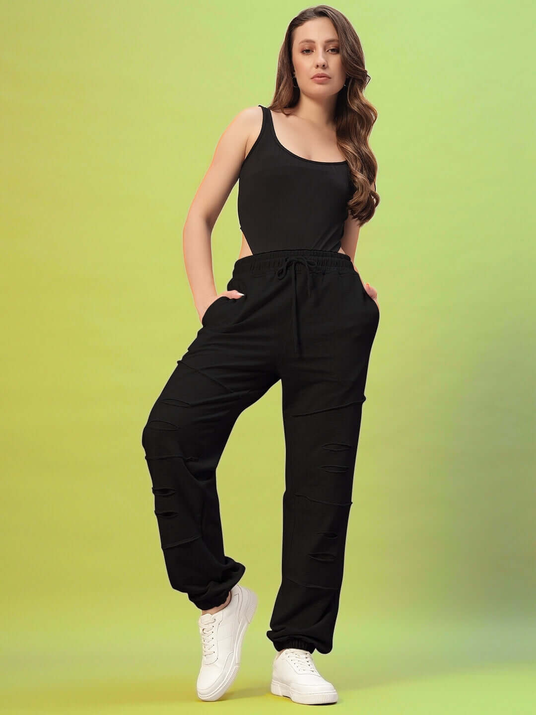 Woman wearing black Women's DUDS Graze Joggers, standing confidently with a green background.