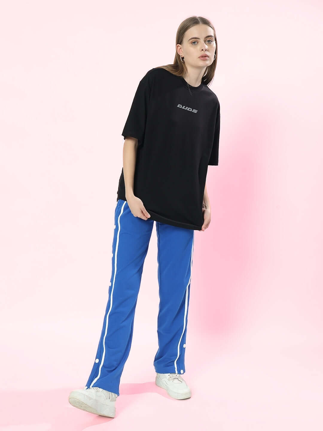 Model wearing black oversized t-shirt 'Pulsating Rhythms Reflector' with blue track pants, showcasing casual fashion style.