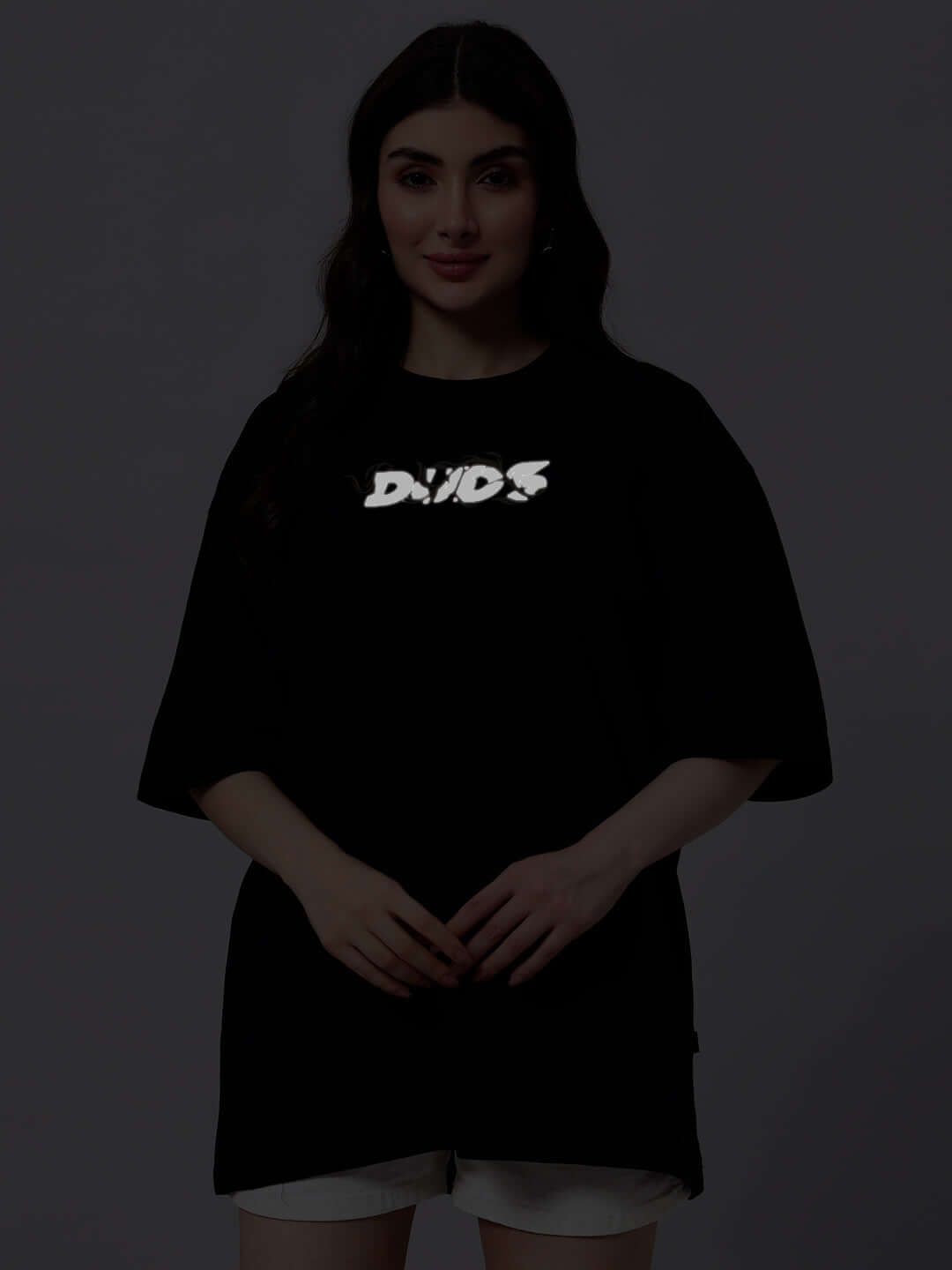 Woman wearing a black oversized t-shirt with white graphic text, made from premium cotton blend. Fashionable casual wear.