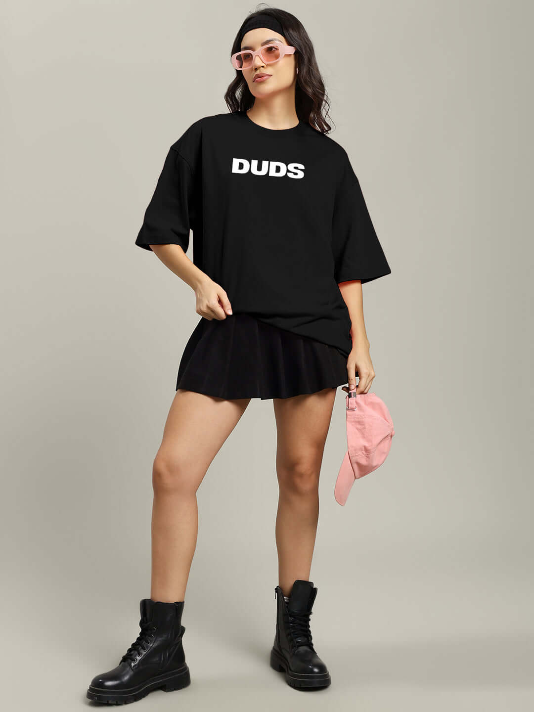 Model wearing a women's oversized black t-shirt with 'Duds' print, styled with a black skirt, boots, and pink accessories.