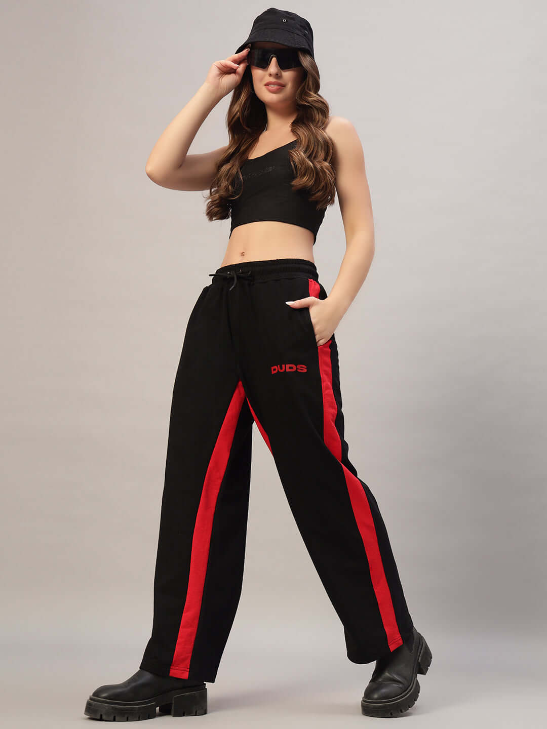 Woman wearing black-red baggy joggers with side seam, styled with a black top, hat, and sunglasses. Perfect blend of comfort and style.