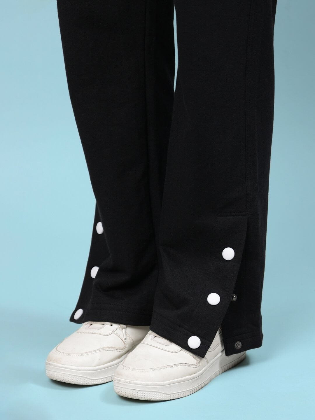 Close-up of WOMEN'S WESENT RELAXED-FIT CO-ORD SET BLACK pants with button detail, worn with white sneakers.