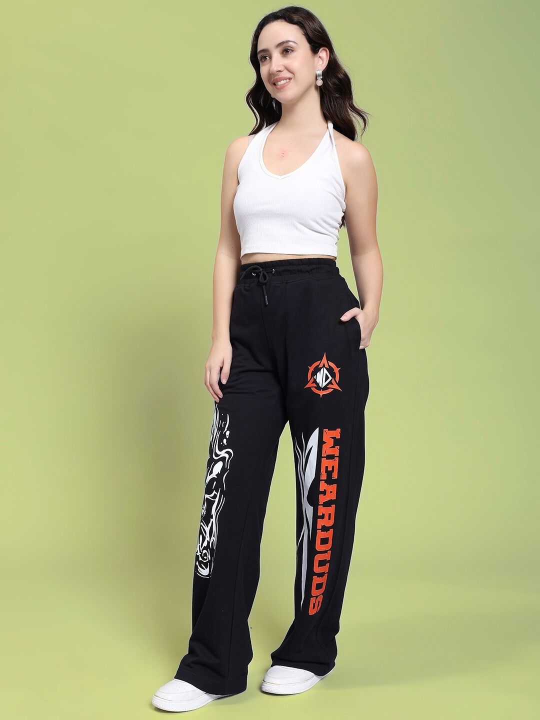 Model wearing WOMEN'S RIFT RELAXED FIT JOGGER IN BLACK with graphic design, standing against a green background.