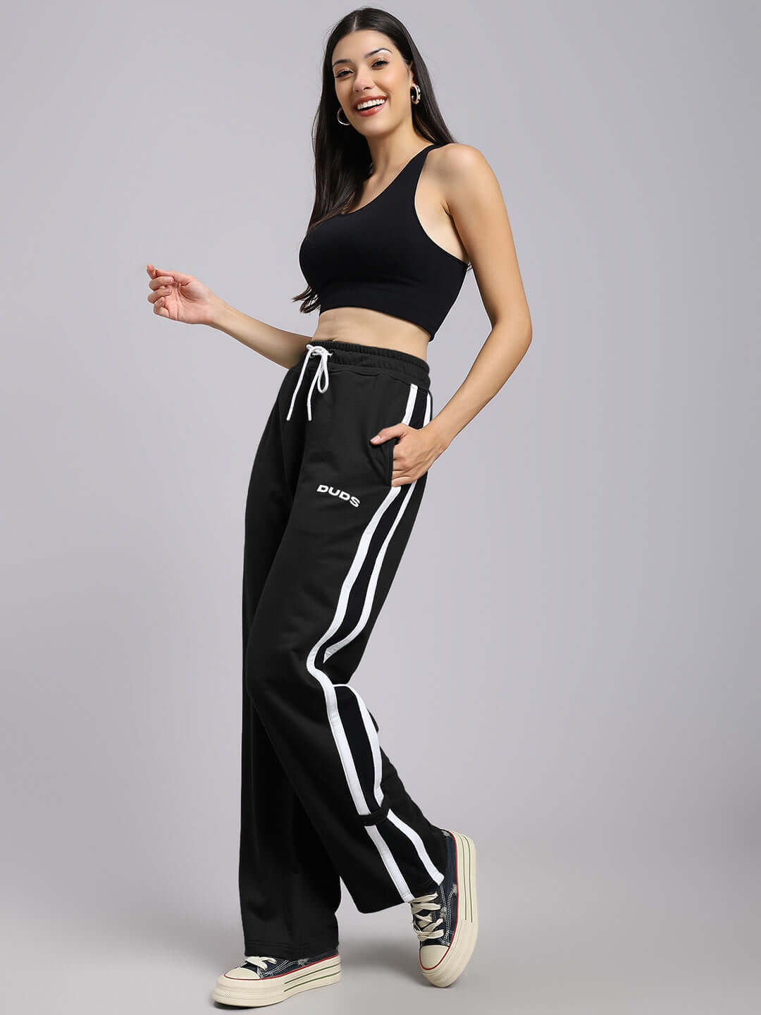 Woman wearing black Rosston joggers with white stripes, featuring relaxed fit and "DUDS" logo, paired with a black crop top.