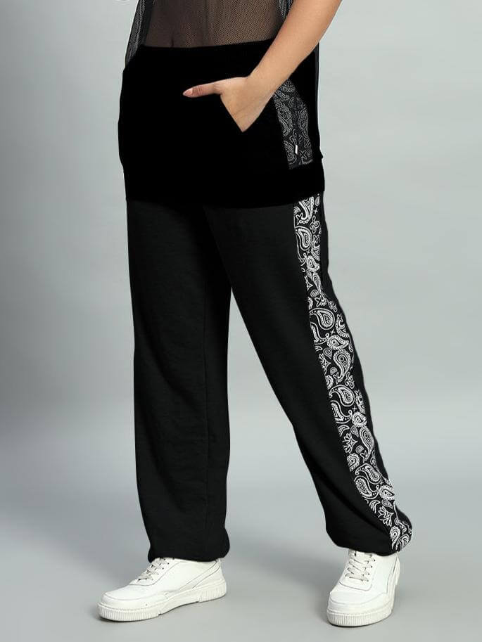 Woman wearing black relaxed fit joggers with paisley print side stripe, paired with white sneakers.