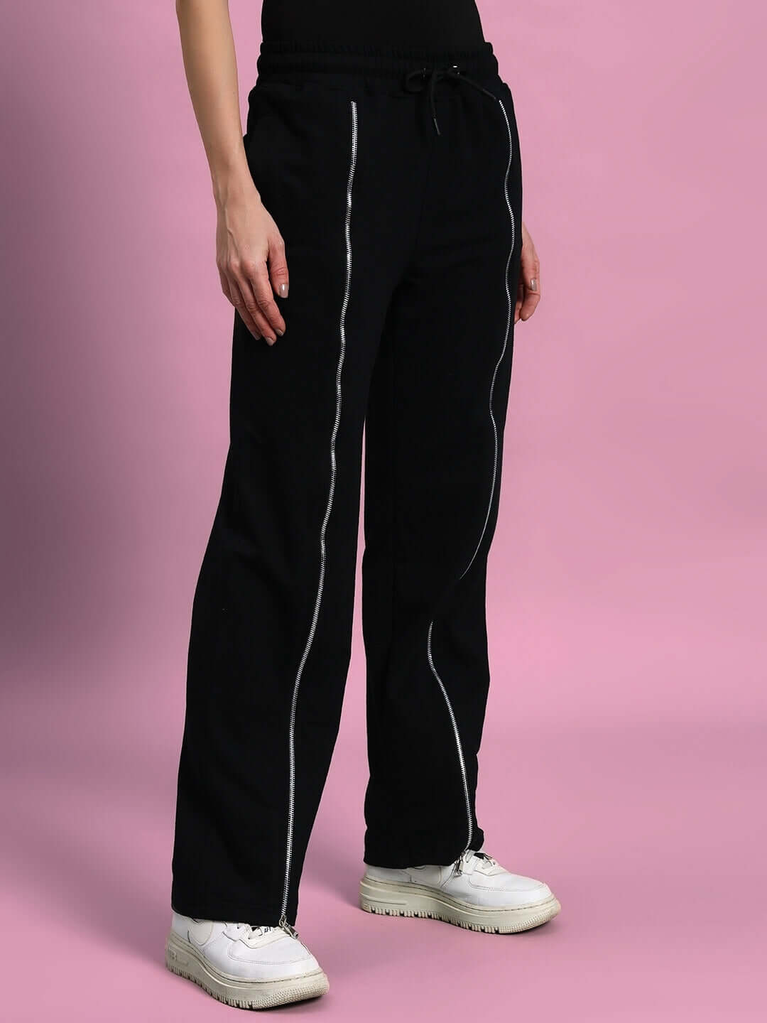 Women's black front open zipper joggers with drawstring, styled with white sneakers on a pink background.