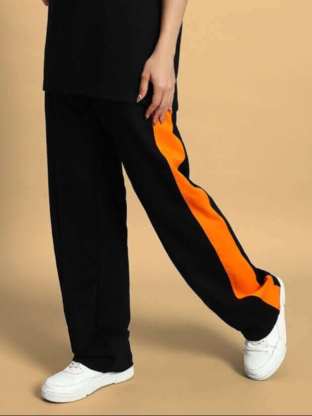 Woman wearing black joggers with orange side contrast stripe, styled for comfort and customization, paired with white sneakers.