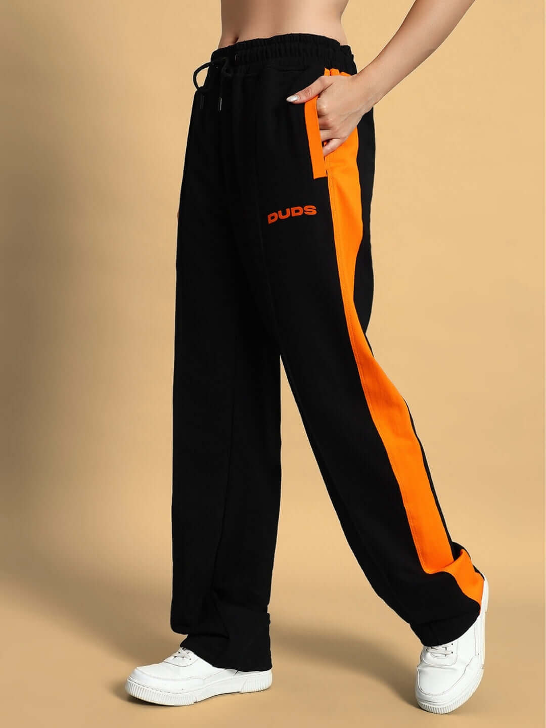 Black joggers with orange stripe, elastic waistband, and pockets, styled with white sneakers. Fashionable unisex relaxed fit.