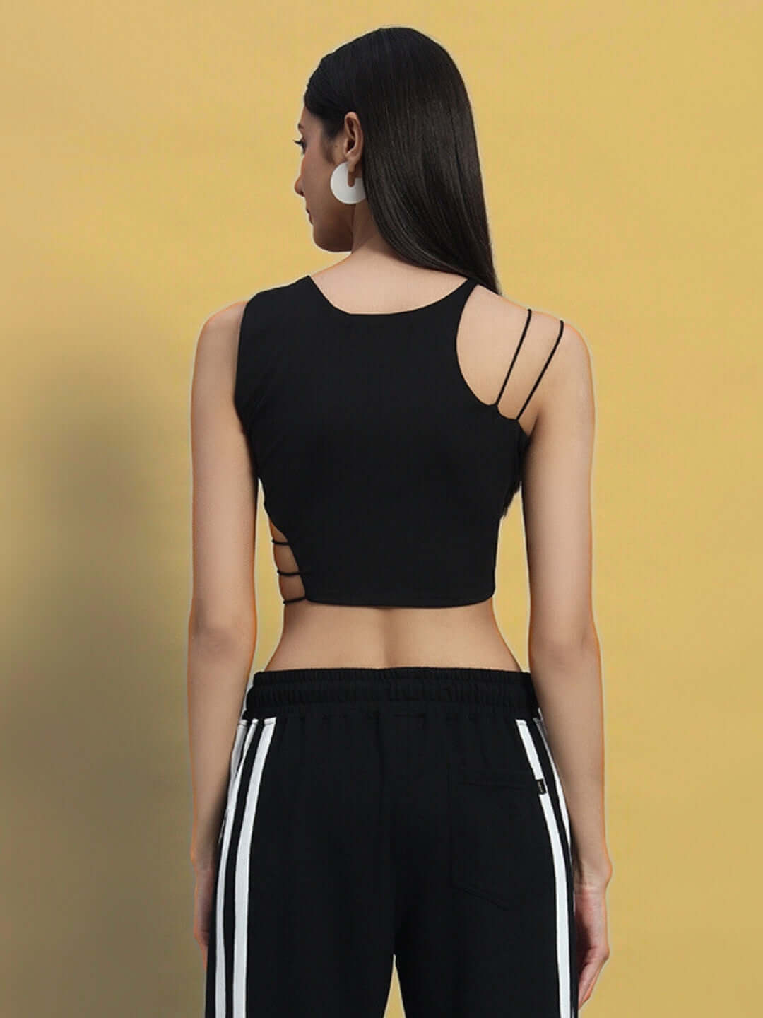 Back view of a woman's stylish black crop-top made from 100% cotton heavy gauge fabric, paired with track pants, showcasing side strap details.