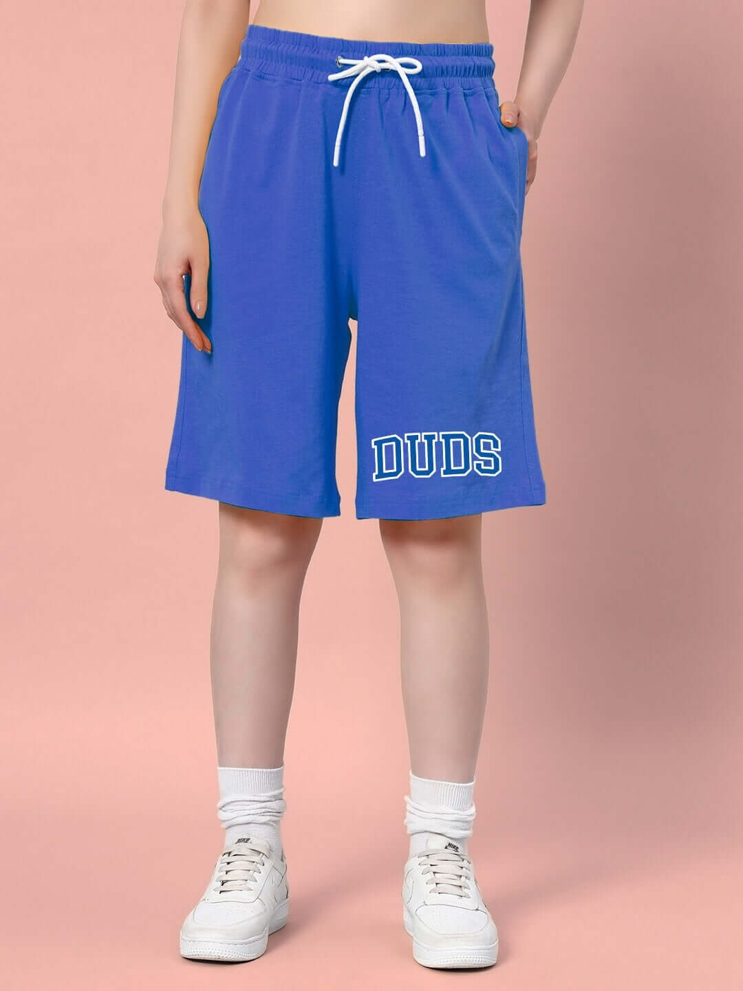 Women's blue summer shorts by DUDS with custom fit options, shown with white sneakers on a light pink backdrop, ideal for warm weather.