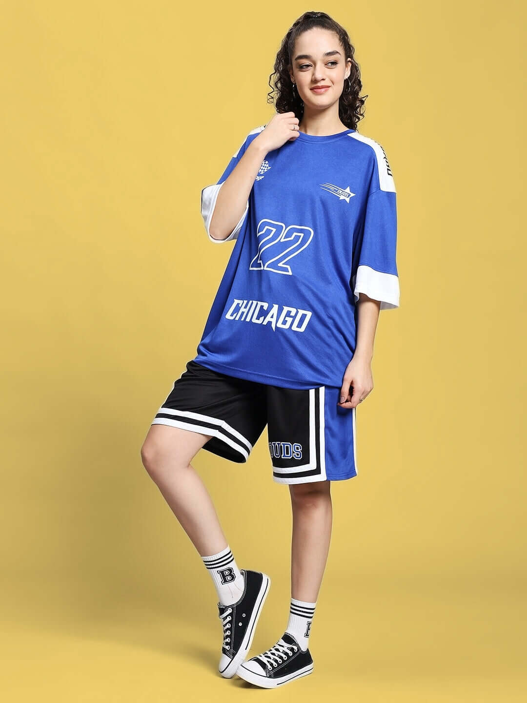 Woman wearing a blue and white sports jersey with the number 22, paired with black and white shorts, posing confidently on a yellow background.