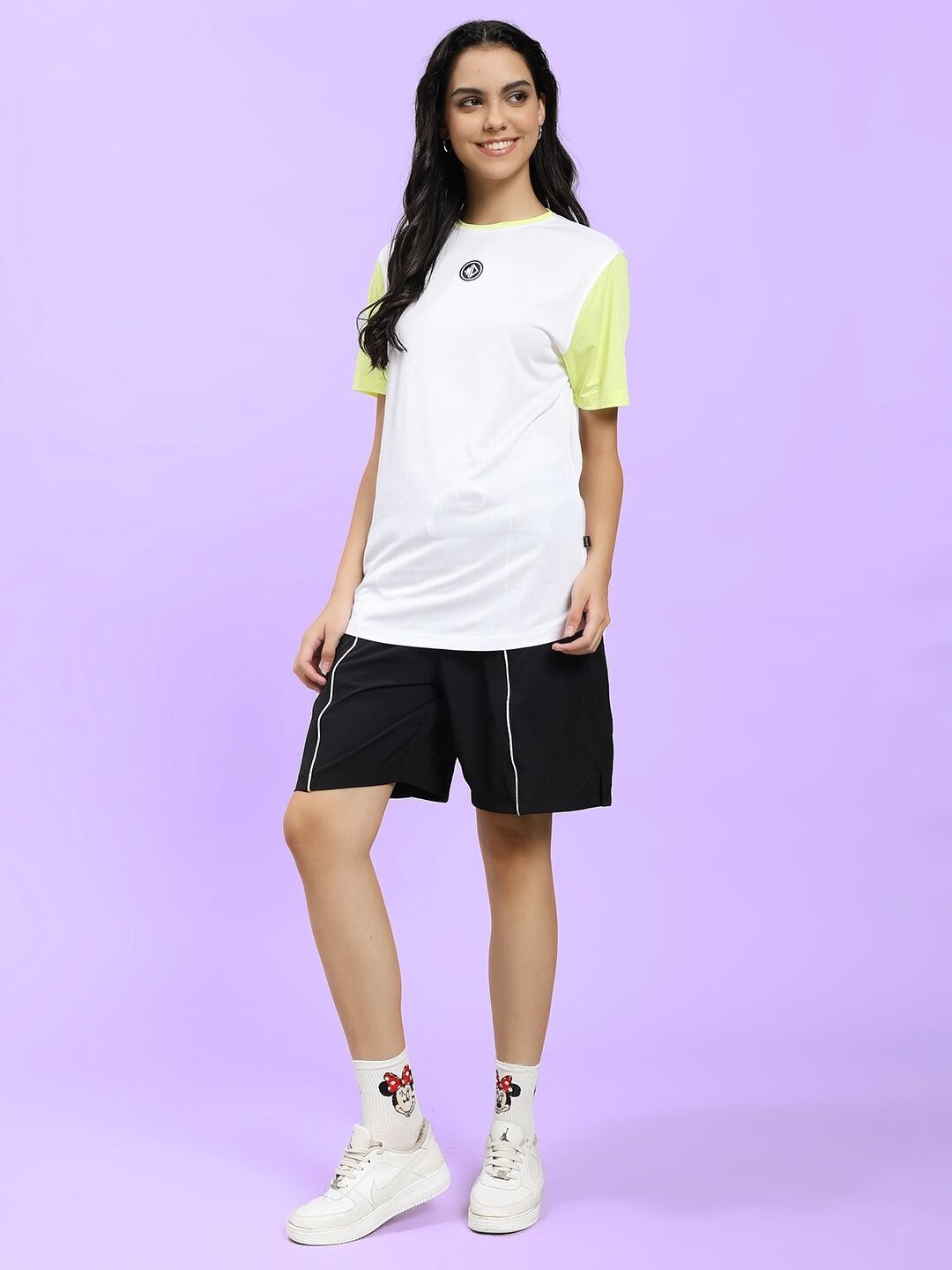 Woman wearing WOMEN CHAMPION ZONE REGULAR FIT CO-ORD WHITE NEON BLACK set, showcasing sporty style and comfort against a purple backdrop.
