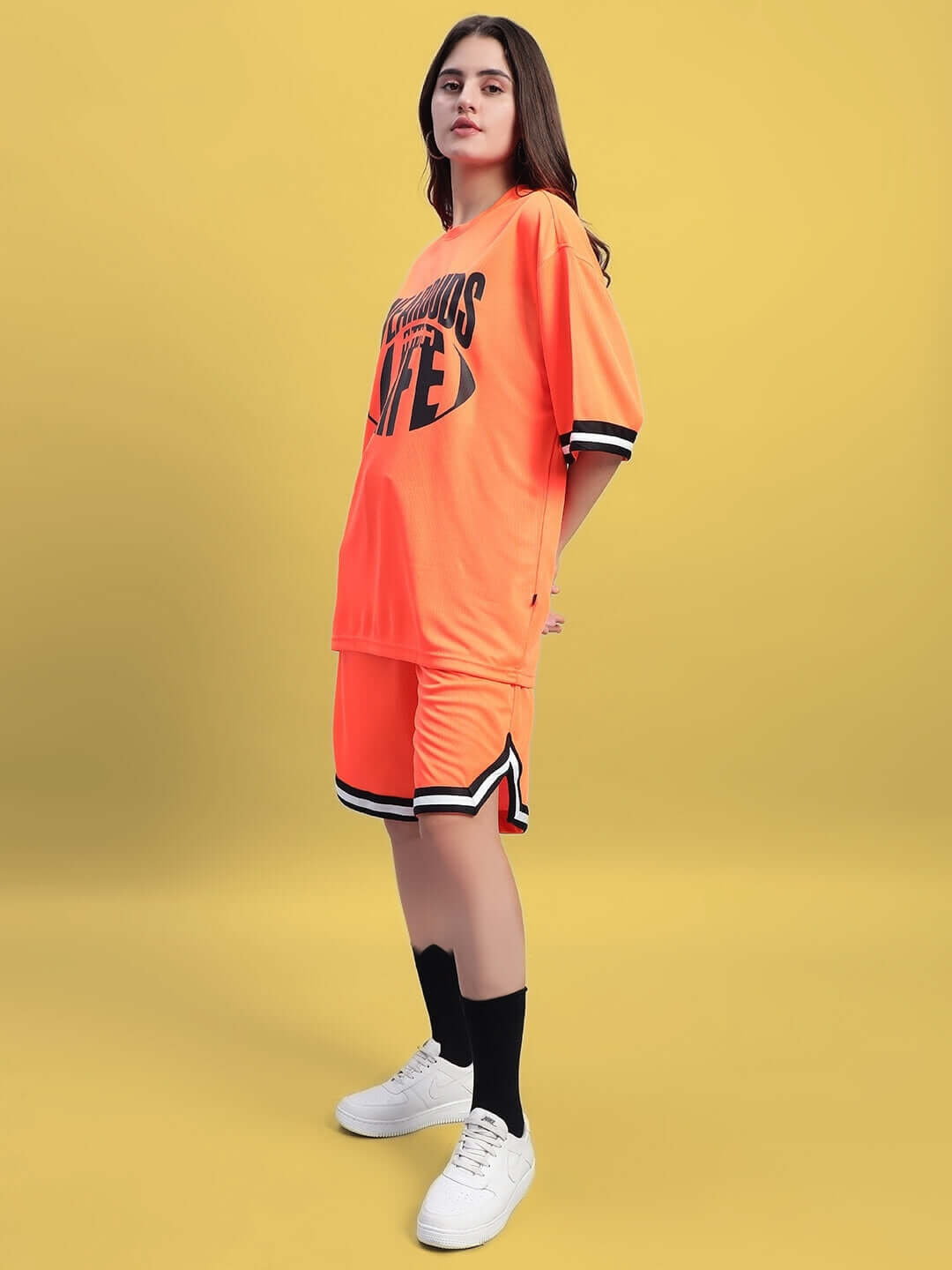 Model wearing WOMEN'S CHRONIC COLORBLOCK CO-ORD SET ORANGE with bold lettering on a vibrant yellow background.