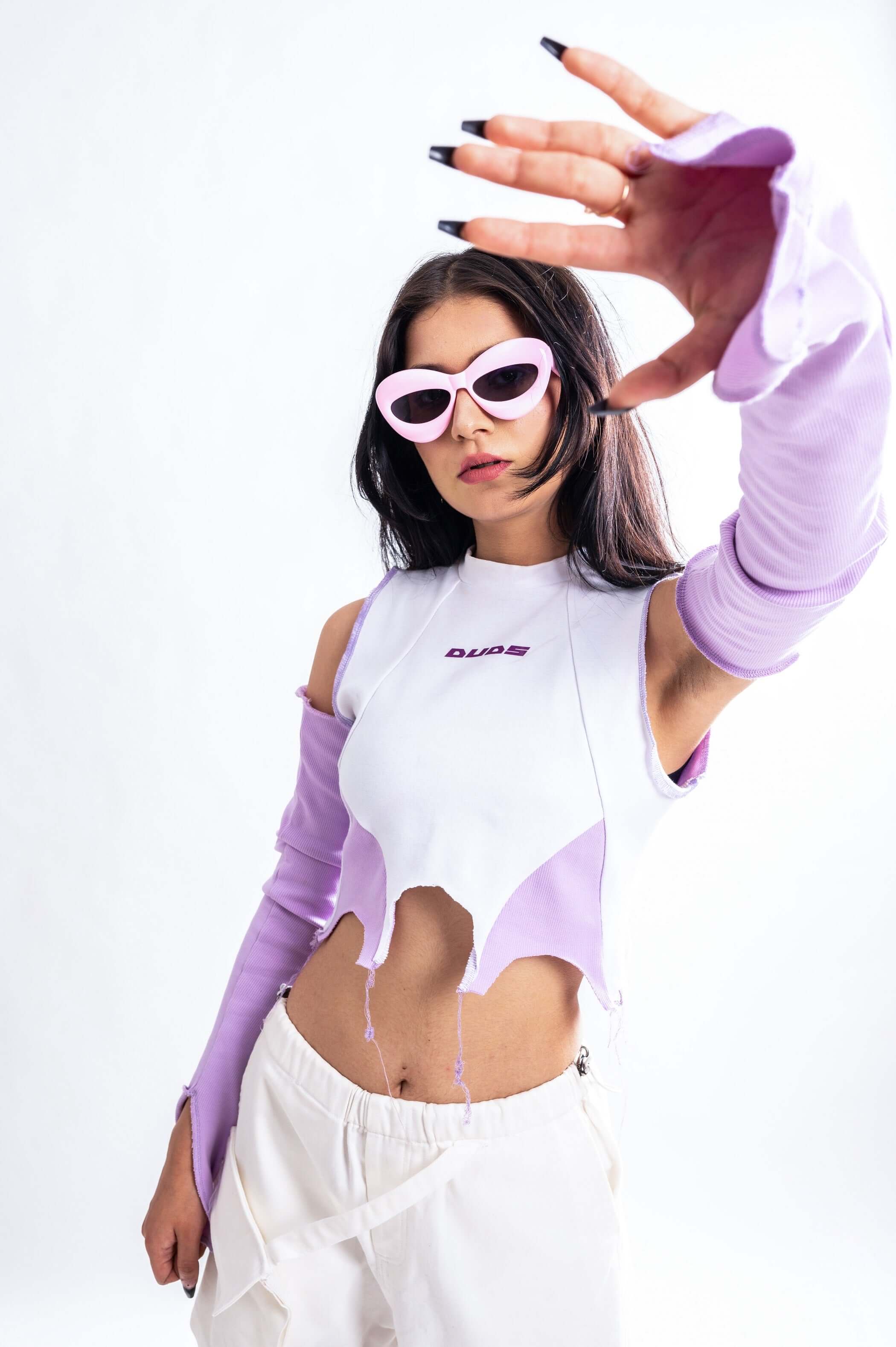 Fashion-forward woman in a white and purple crop top with long sleeves, showcasing a trendy look with stylish sunglasses.