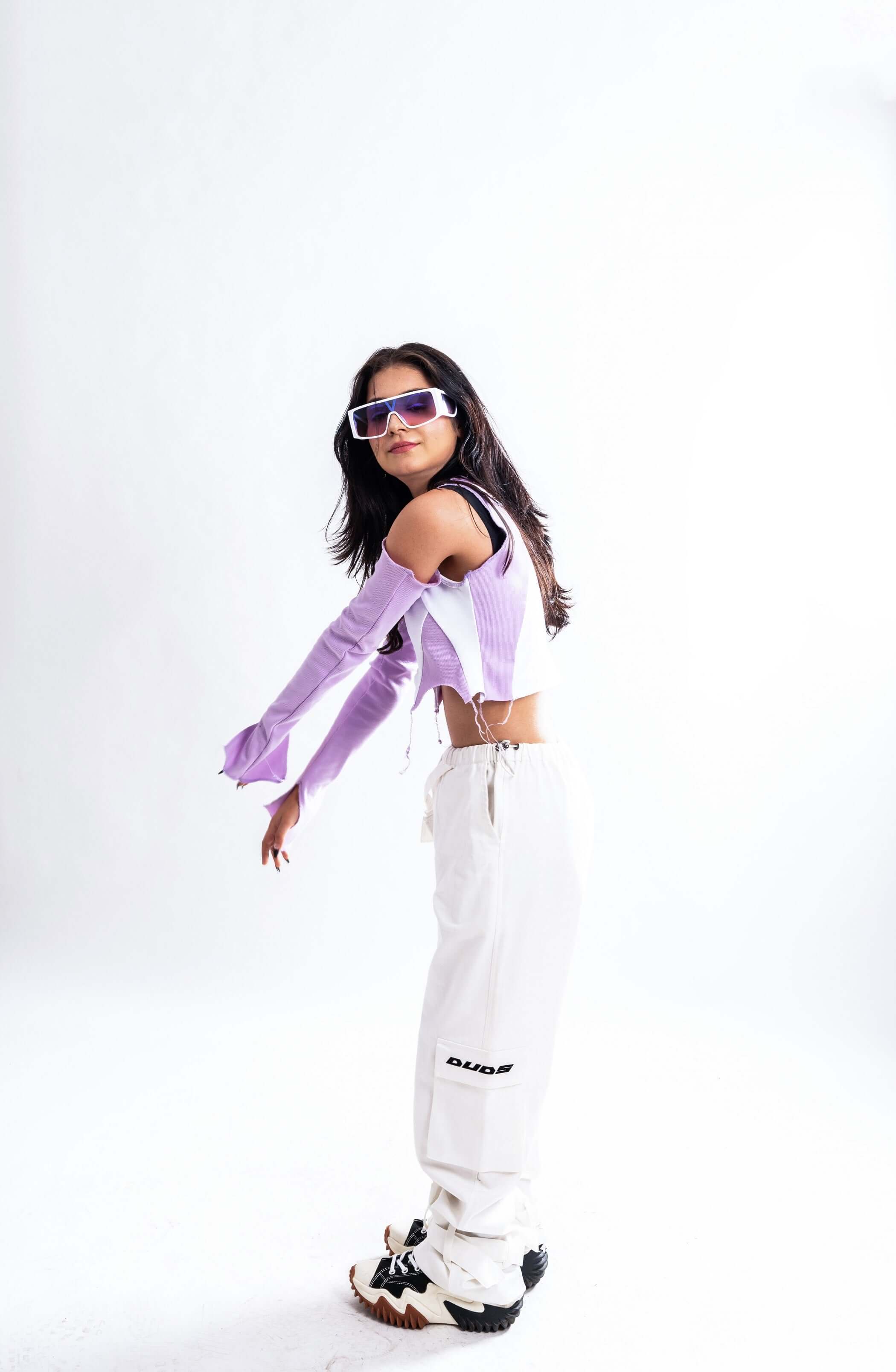 Model in purple color block crop top with long sleeves and white pants, showcasing trendy women's fashion.