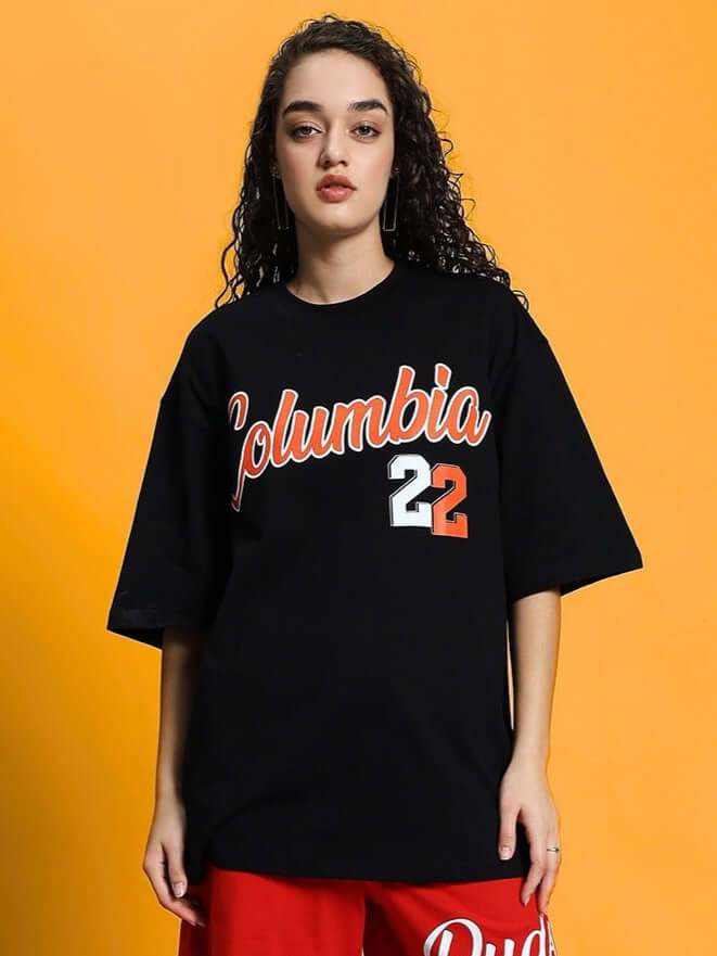 Woman wearing a black oversized Columbia 22 print T-shirt in premium cotton fabric against an orange background.