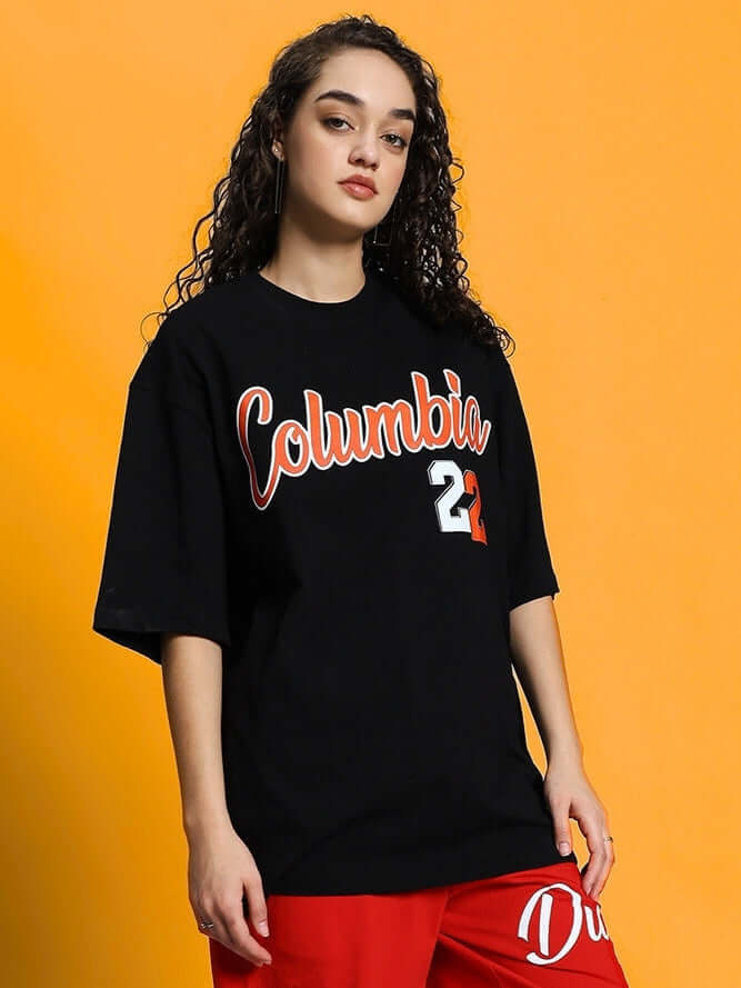 Woman wearing Women's Columbia 22 black oversized t-shirt made of premium cotton fabric standing against an orange background