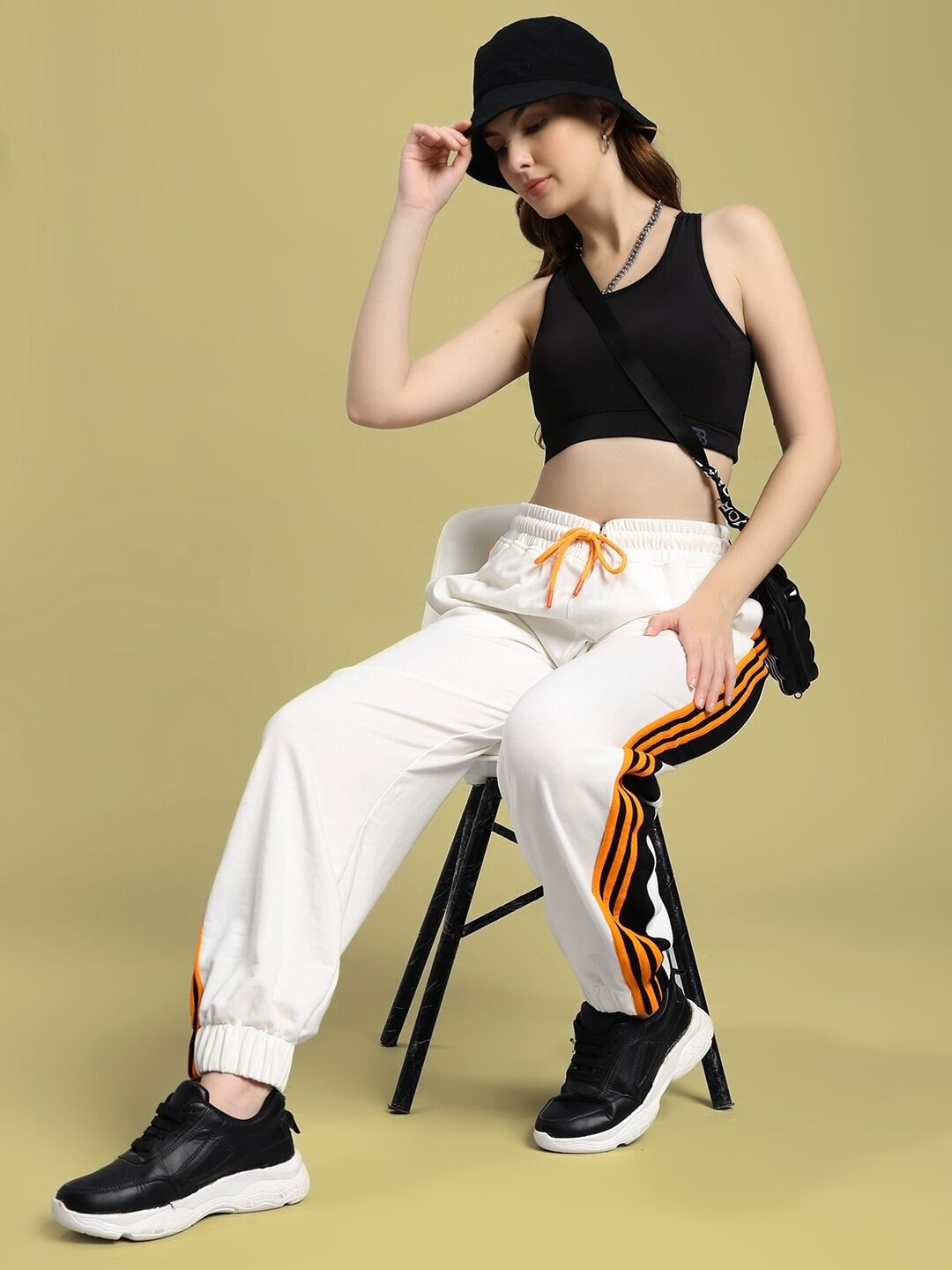 Woman wearing WOMEN'S COMFORT FLEX STRIPE JOGGER OFF-WHITE with black top and sneakers, seated on chair, showcasing modern casual style